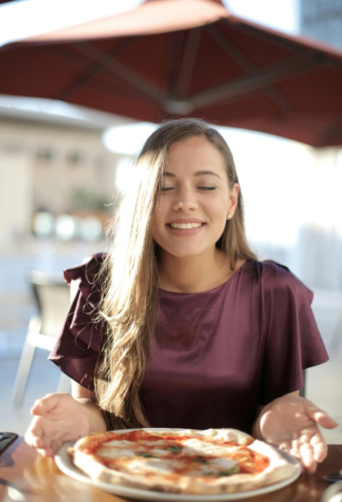 Young woman smiling while savoring a tasty Italian pizza at an outdoor cafe.